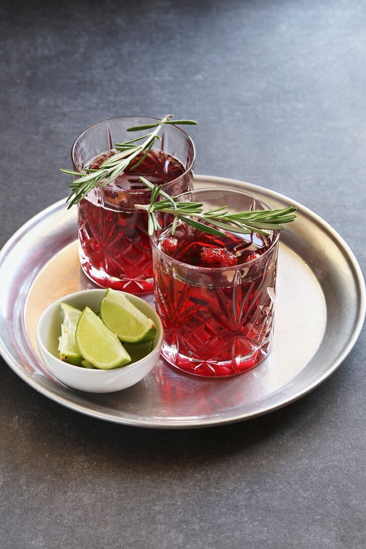 Cranberry-Cocktail mit Rosmarin garnieren in Gläsern auf Tablett