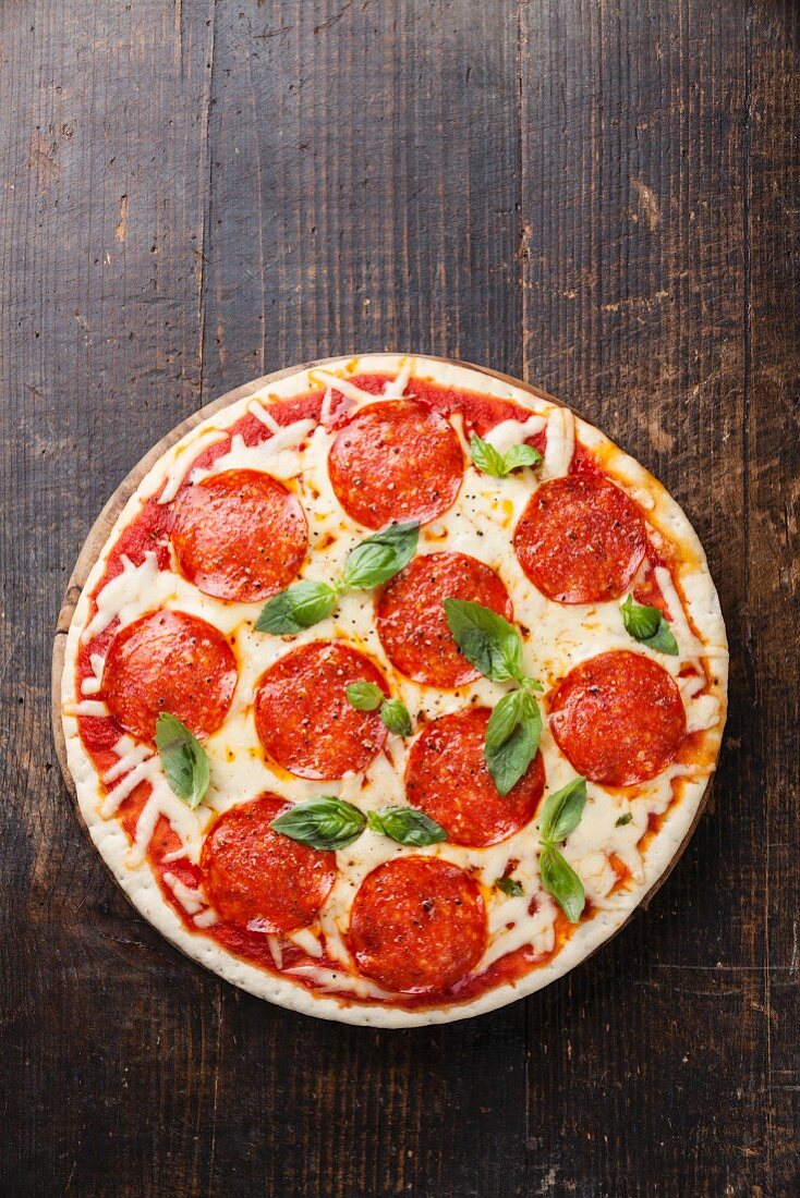 Pizza mit Pepperoni-Salami und Basilikum auf Holztisch