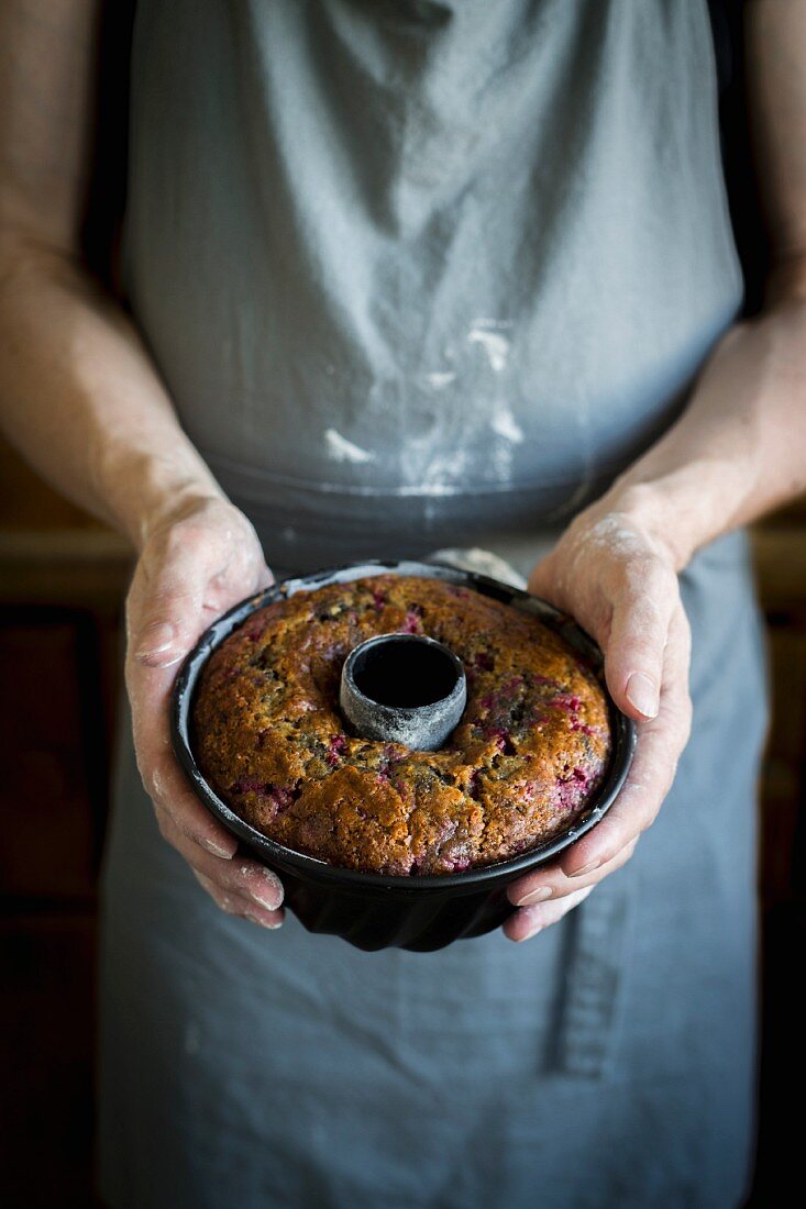 Person with kitchen apron and floured hands holding bundt cake in baking dish