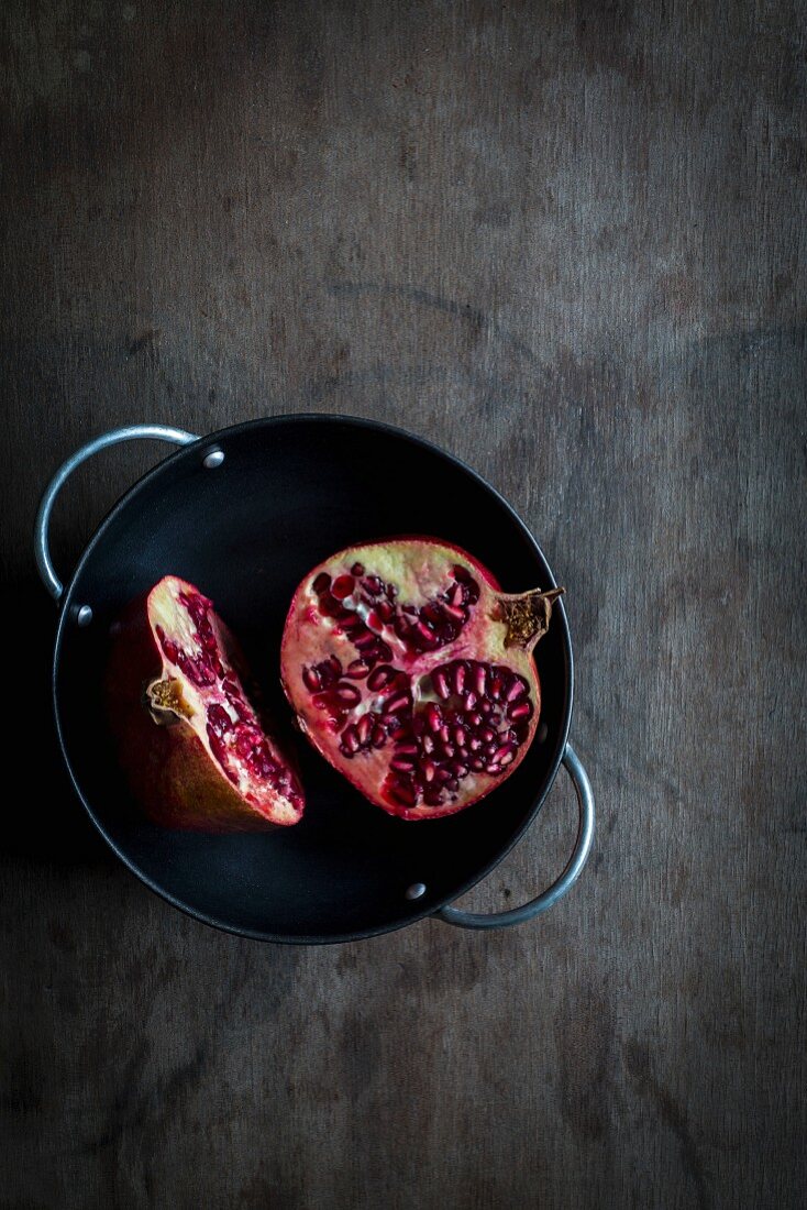 Pomegranate cut in halves in black bowl on wooden tabletop