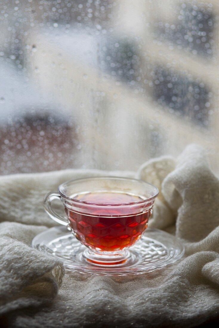 Glastasse mit Tee vor einem verregnetem Fenster