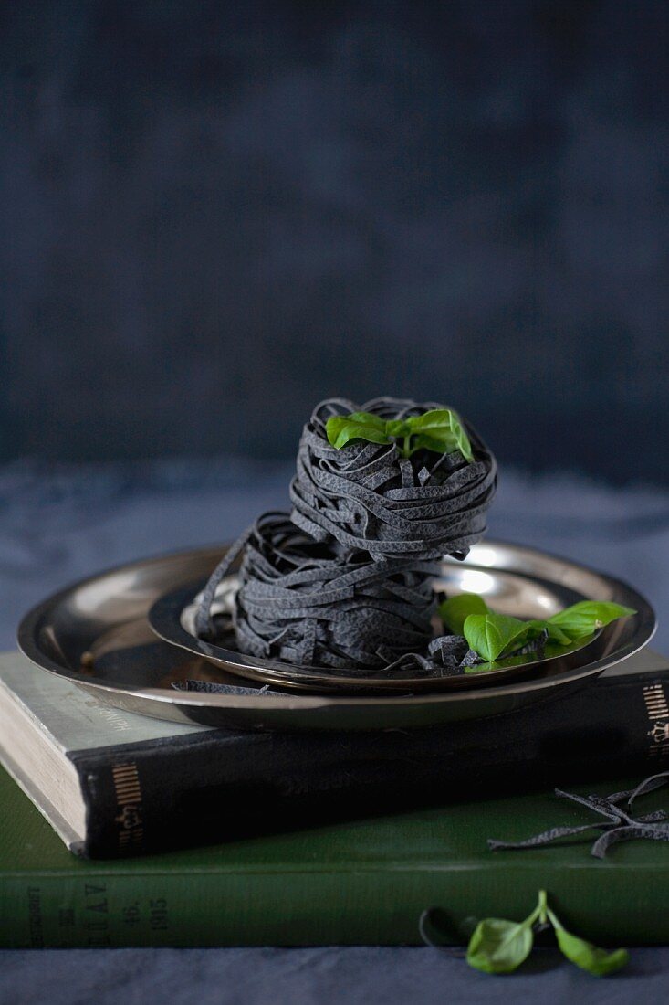 Black ribbon noodles and basil leaves on a metal plate