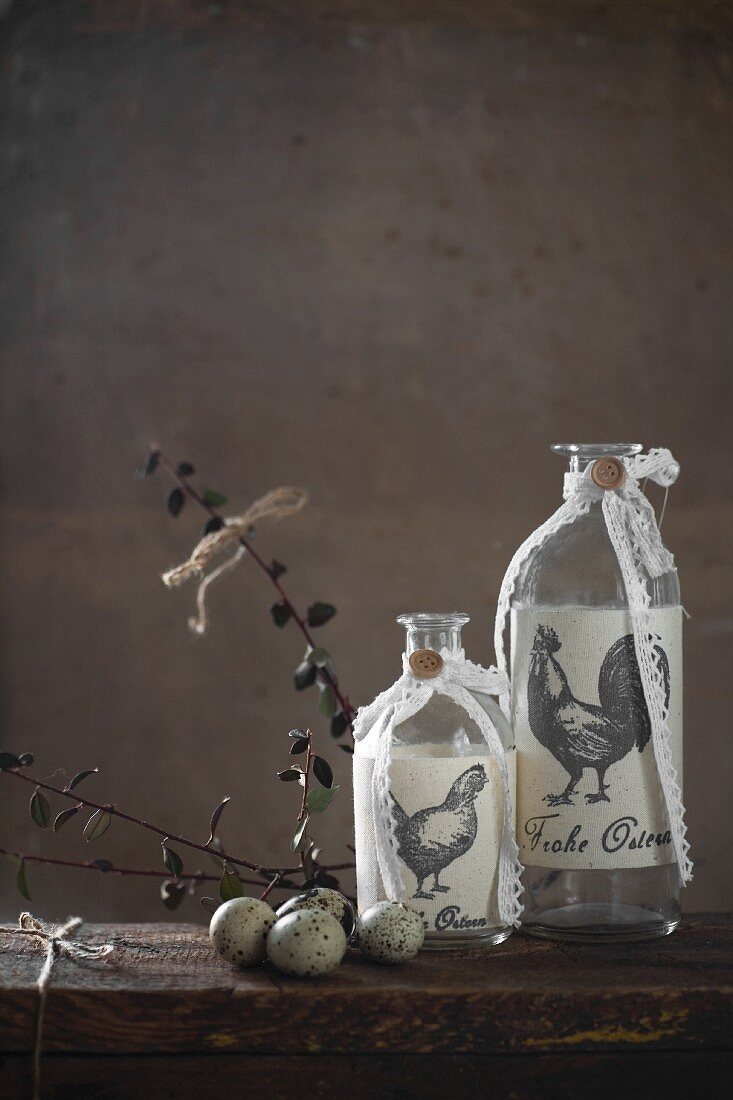 Decorated glass bottles and quail eggs on wooden table in front of grey wall