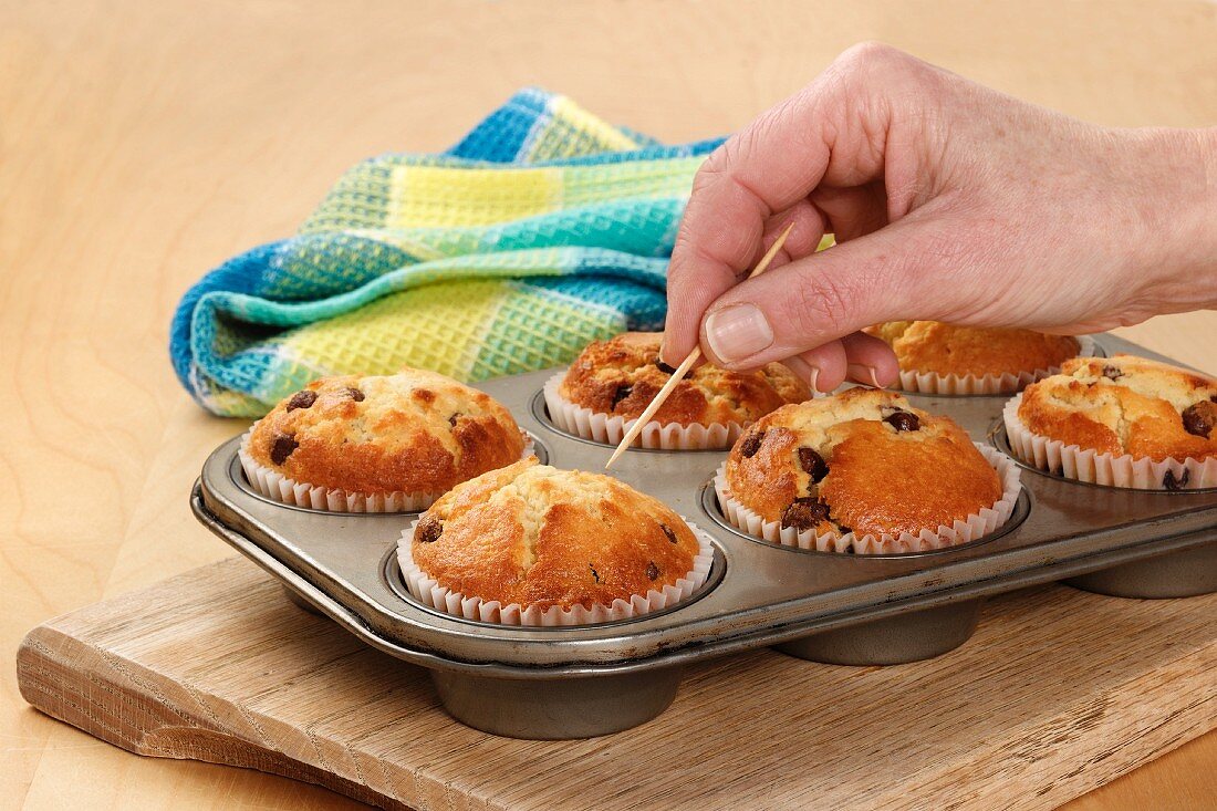 Someone testing, with a toothpick, if cupcakes in a baking tray are fully cooked