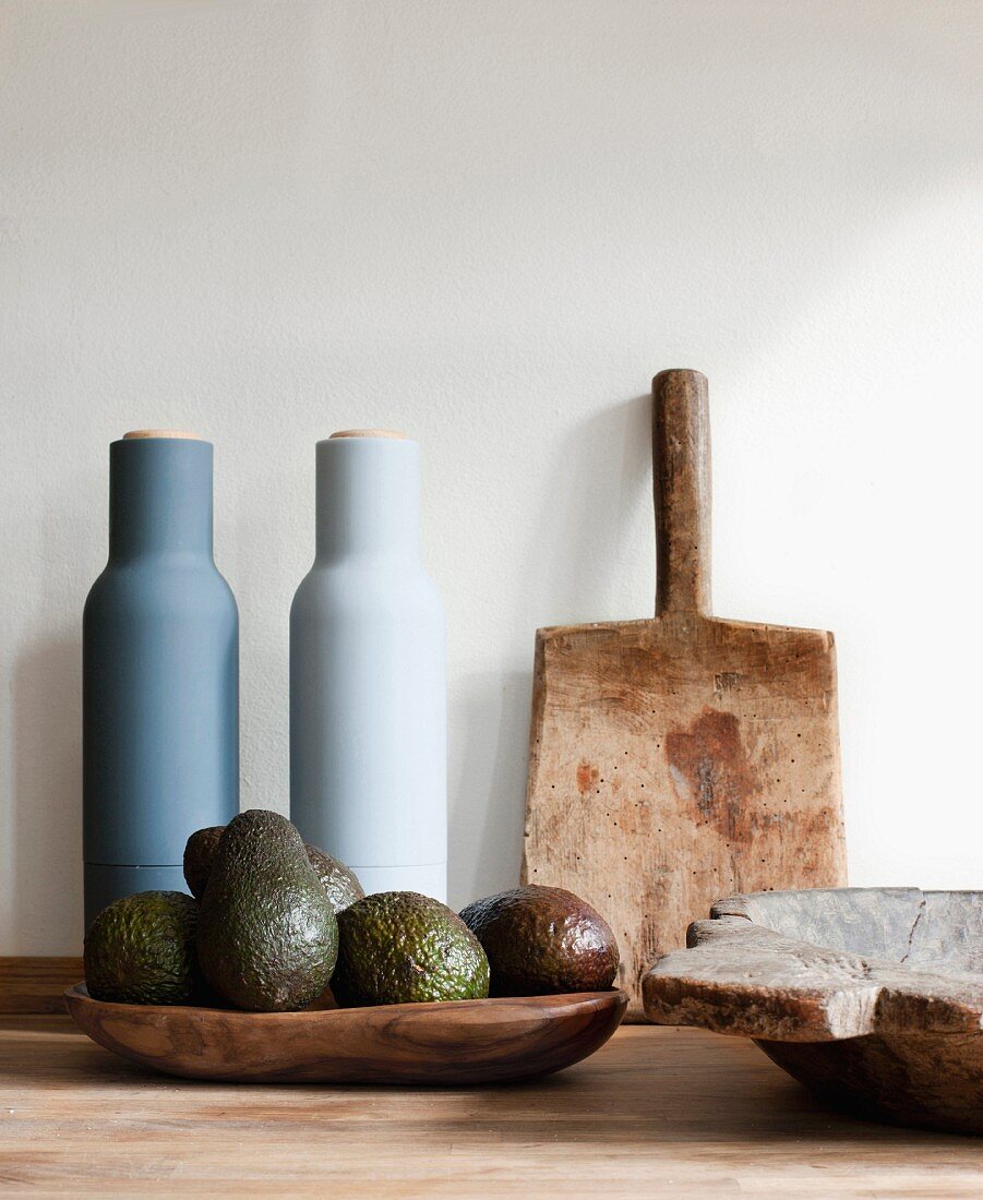 Ecology and Soft Colours. Close up of a wooden board, a wooden bowl of avocados and two pottery jars