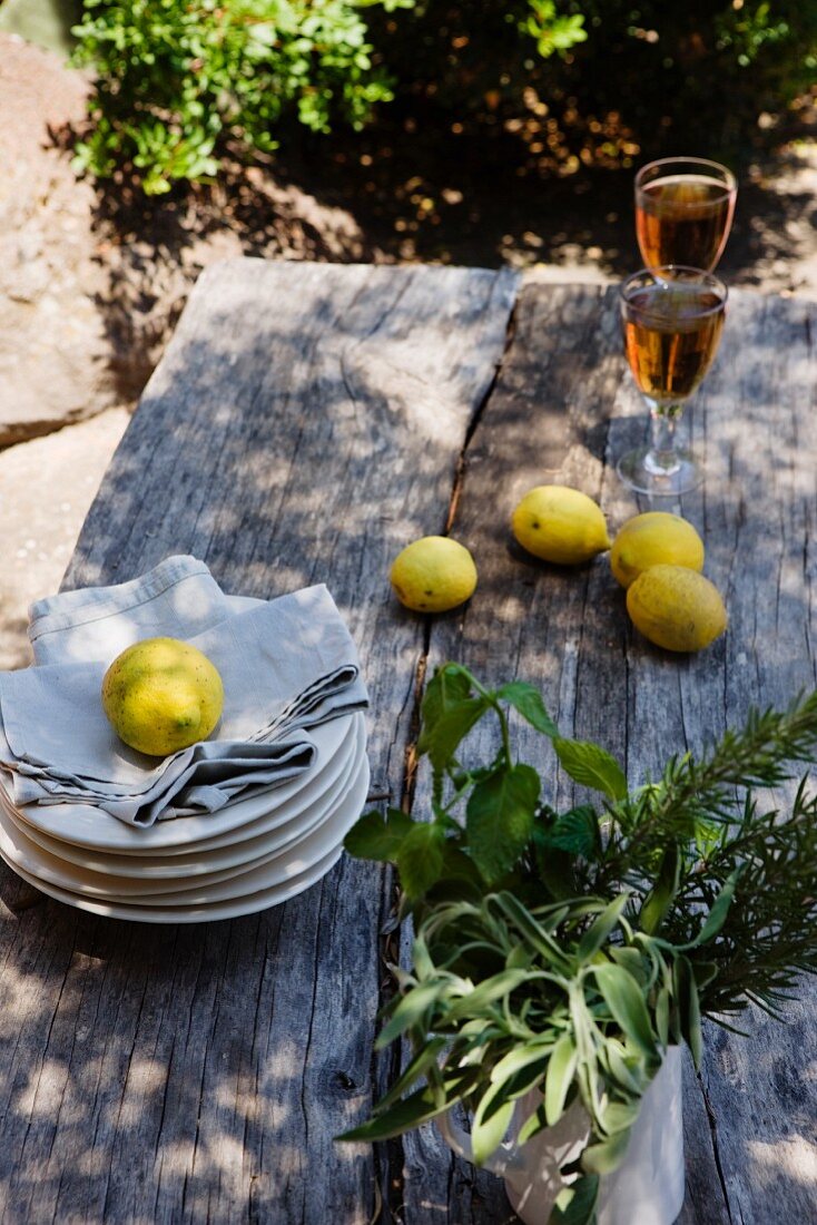 Lemons, pile of plates and serviettes and glasses of white wine on rustic wooden table
