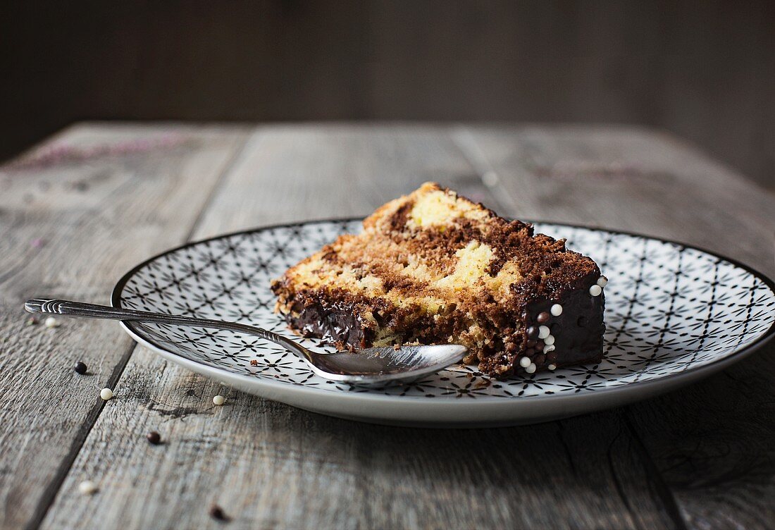 Ein Stück Marmor-Chiffon-Cake mit Schokoladenglasur auf grauem Holztisch
