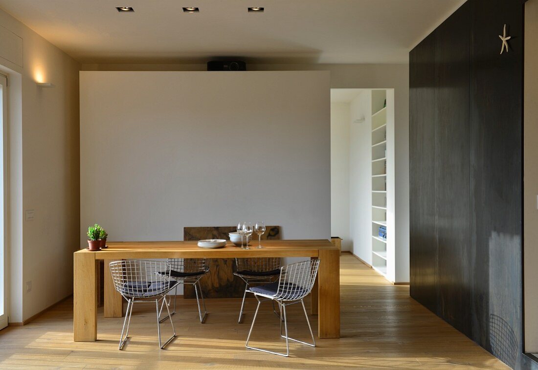 Solid-wood dining table and metal chairs against white partition with open doorway and black metal cladding to one side