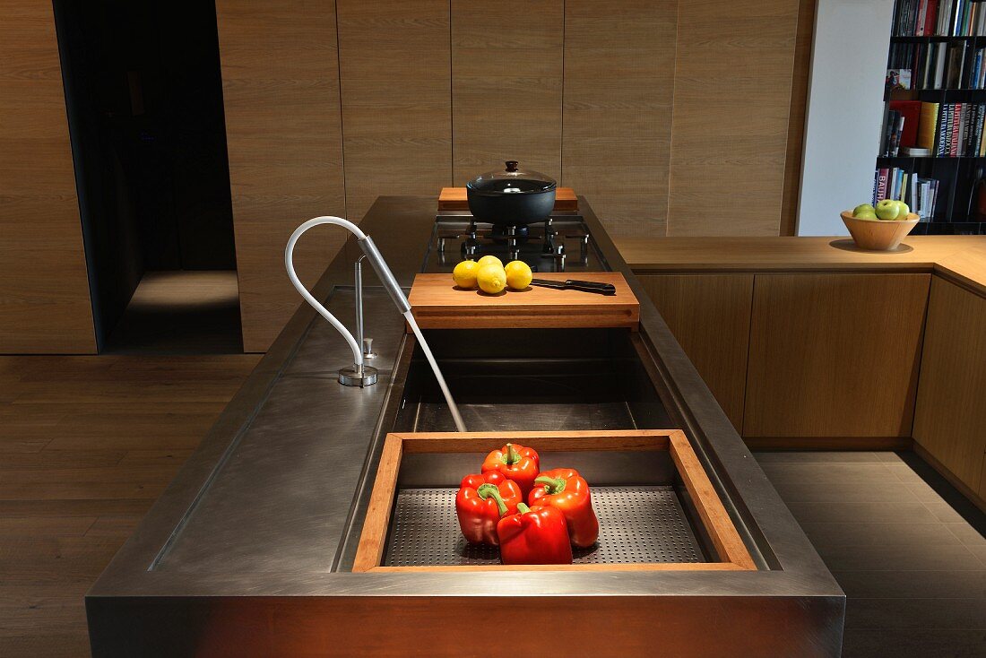 Modern, metal counter with integrated wooden chopping board and gas hob in front of simple fitted cupboards