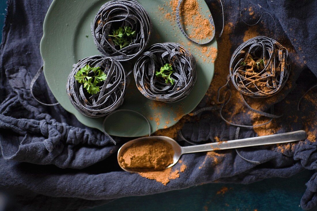 Black ribbon noodles with parsley and spilled spices on a black cloth