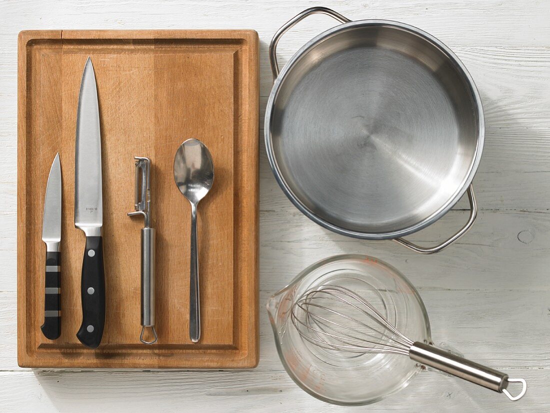 Verschiedene Küchenutensilien: Topf, Messbecher, Schneebesen, Messer, Sparschäler