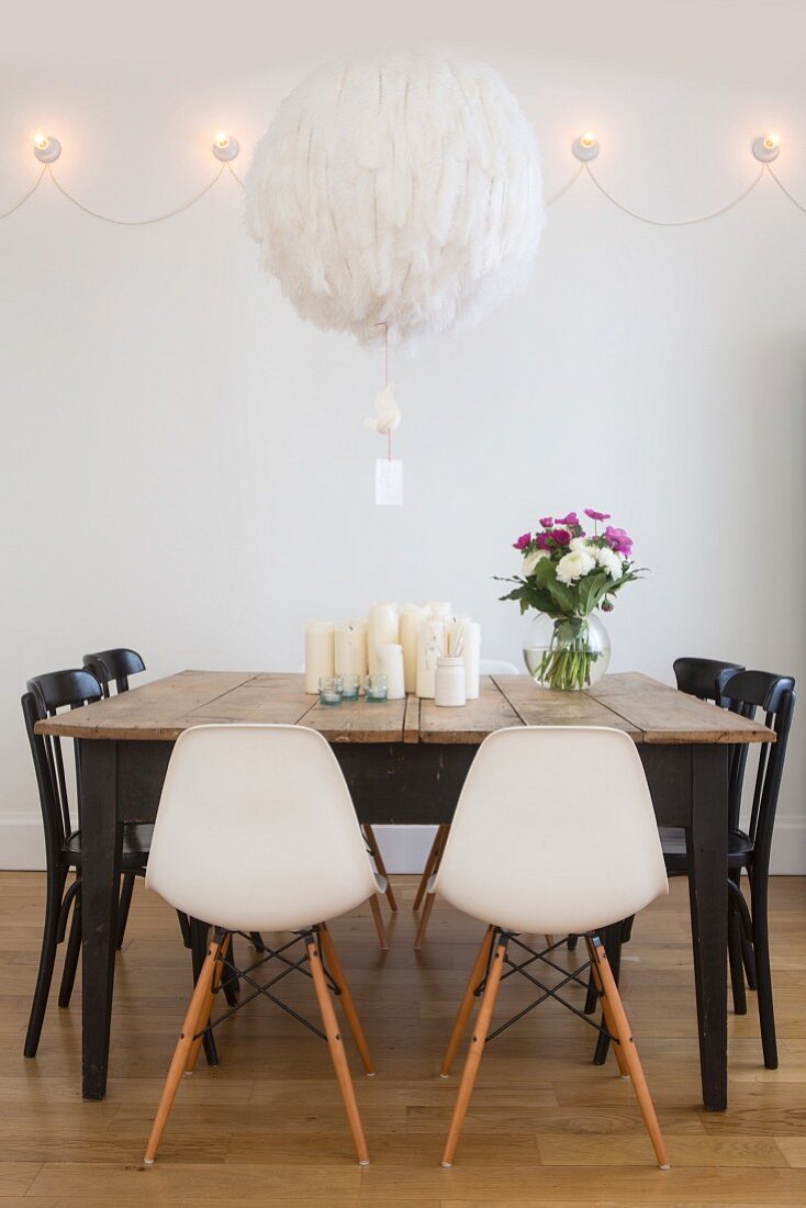 Spherical feathered lampshade above old wooden table with various chairs