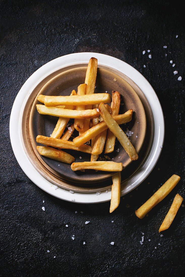 Ceramic plate of french fries with sea salt over black background