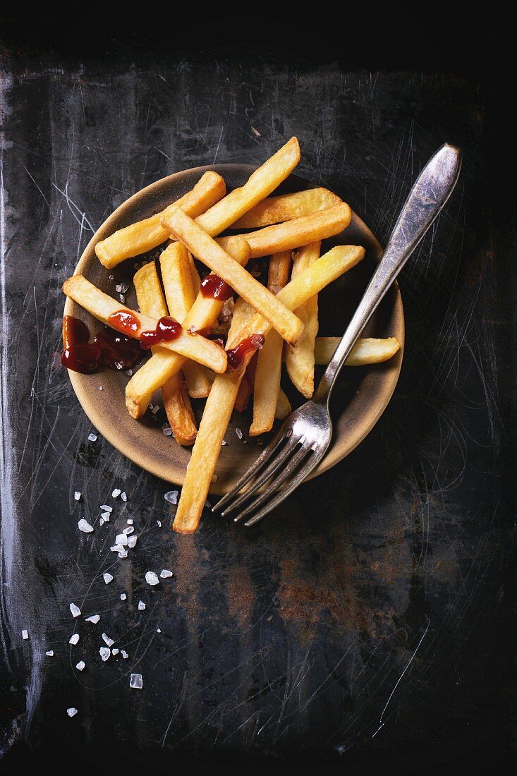 Pommes Frites mit Meersalz und Ketchup auf Teller vor schwarzem Metallhintergrund