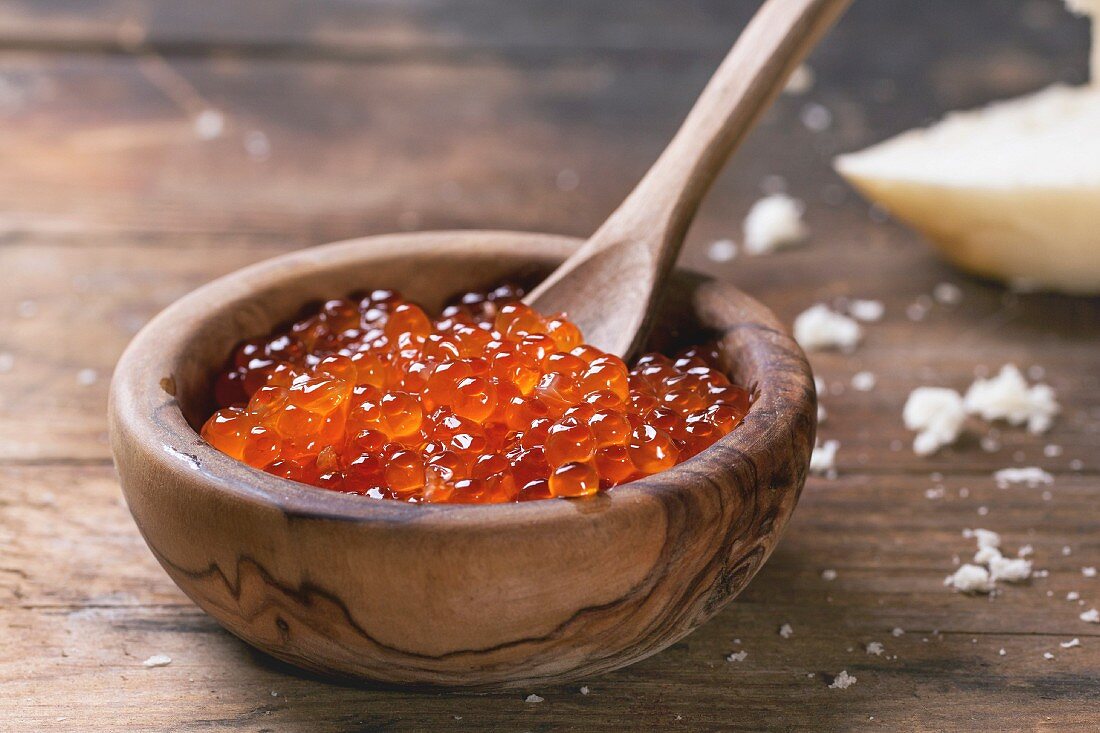 Olive wood bowl of red caviar over old wooden table
