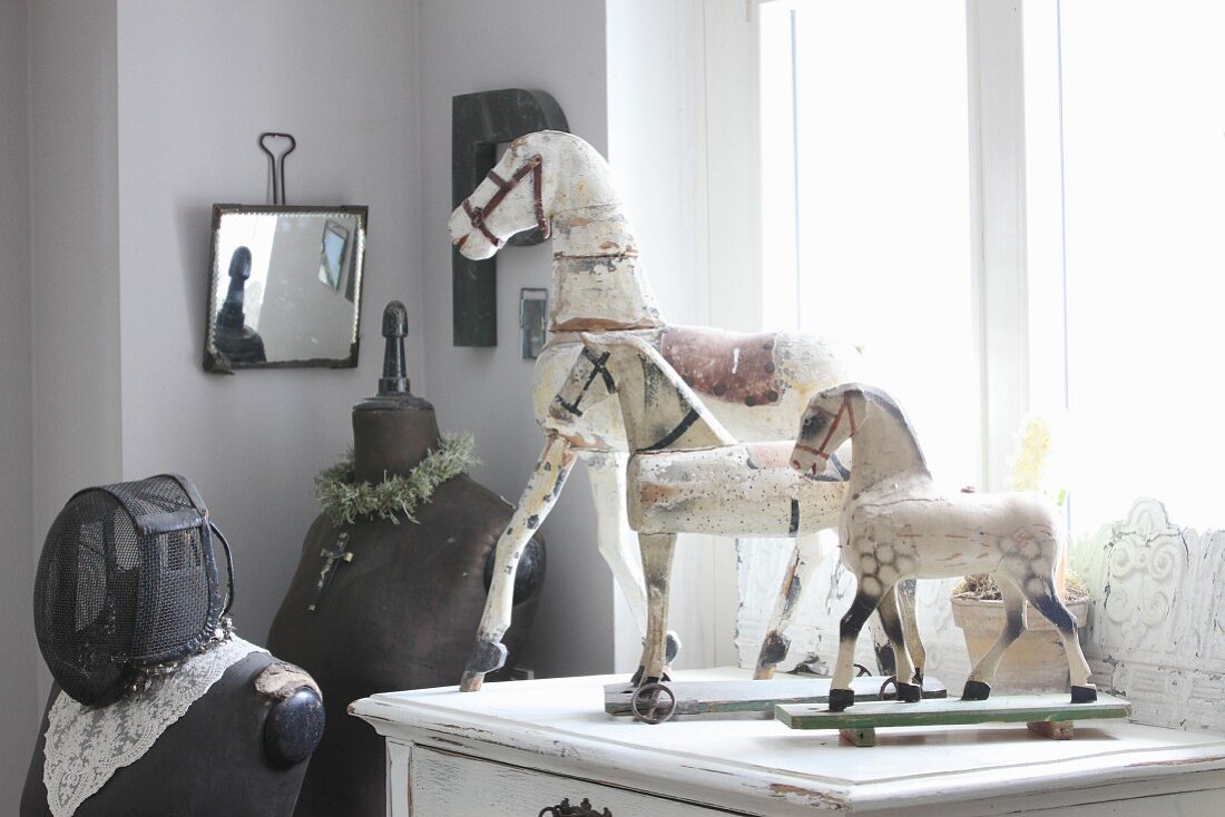 Toy horses on old cabinet next to tailors' dummies