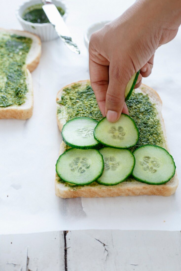 Placing Cucumber slices over spread coriander chutney on the bread