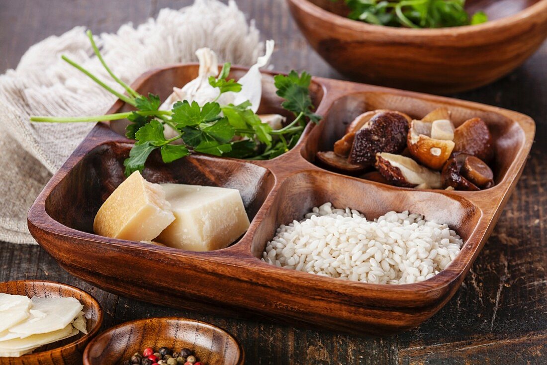 Raw white rice in wooden bowl with ingredients for risotto with wild mushrooms