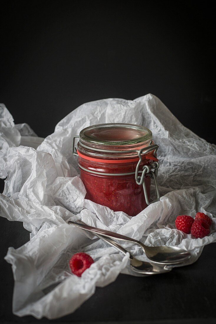 Jar of raw raspberry and chia jam in white paper before dark background