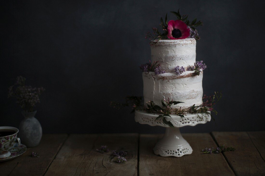 Zweistöckige Torte verziert mit Blüten auf Tortenständer