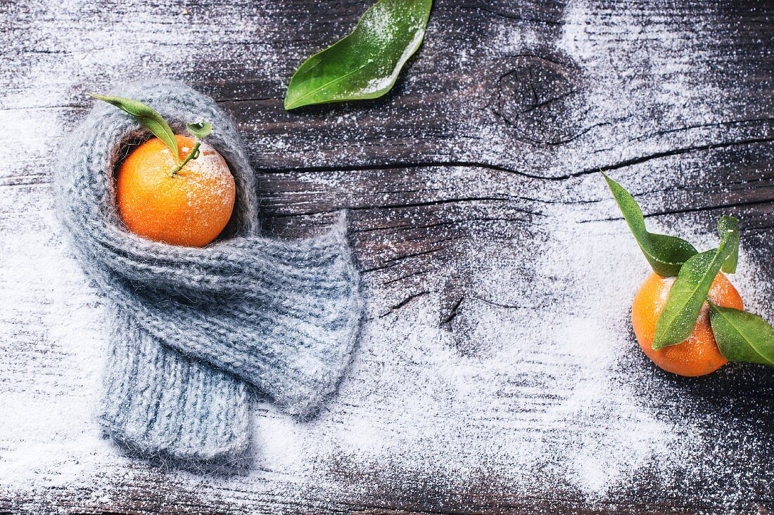 Winterliches Stillleben mit Tangerine in Schal gewickelt auf hölzernem Untergrund mit Schnee