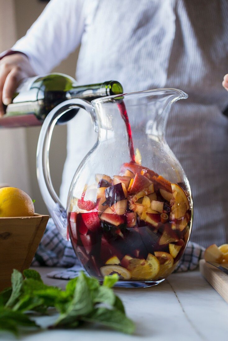 Sangria zubereiten: Wein wird in Glaskrug mit Früchten gegossen