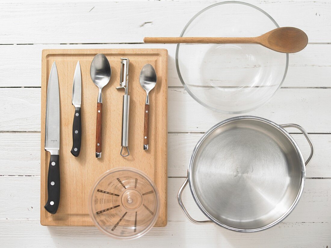 Various kitchen utensils: pot, bowl, measuring cup, knives, spoons, peeler