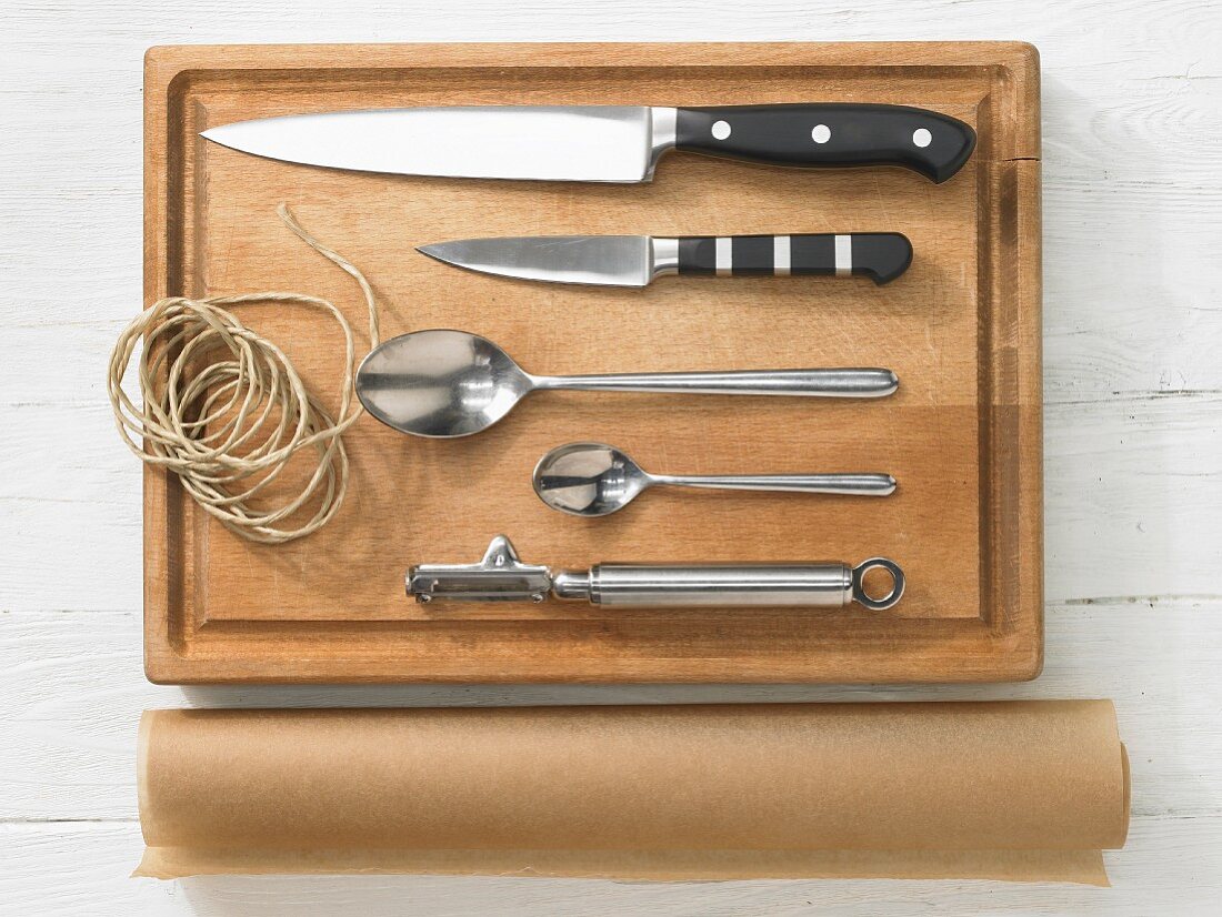 Various kitchen utensils: knives, spoons, peeler, brown string, baking paper