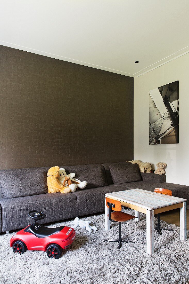Spielsachen im Wohnzimmer mit grauem Sofa vor strukturierter Wand