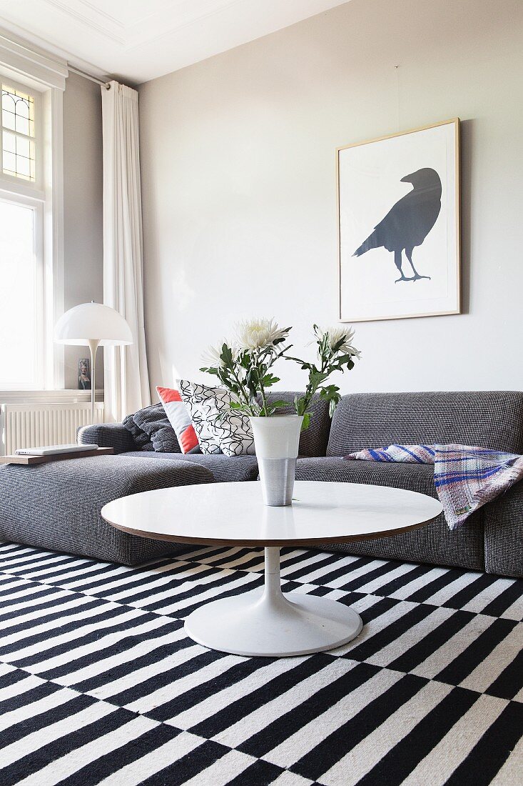 Round coffee table and grey sofa on black and white striped rug