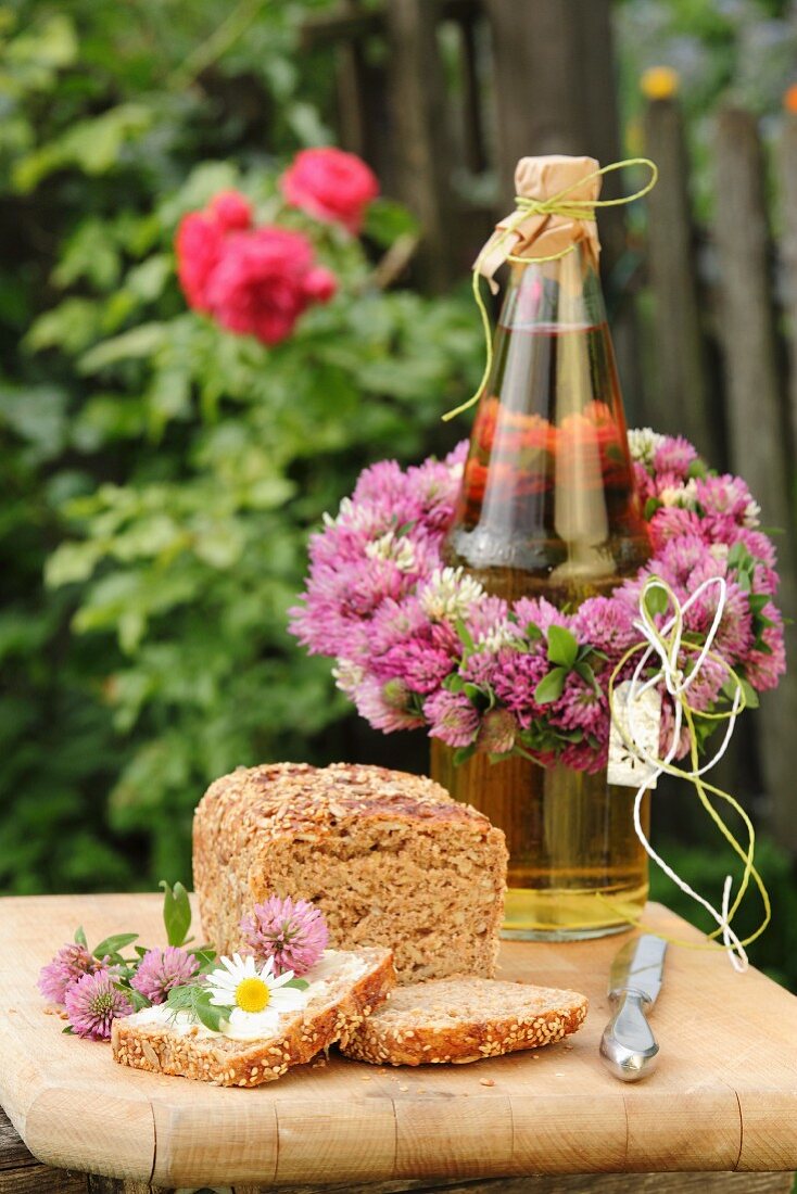 Bottle decorated with wreath of clover flowers, bread and edible flowers on wooden board