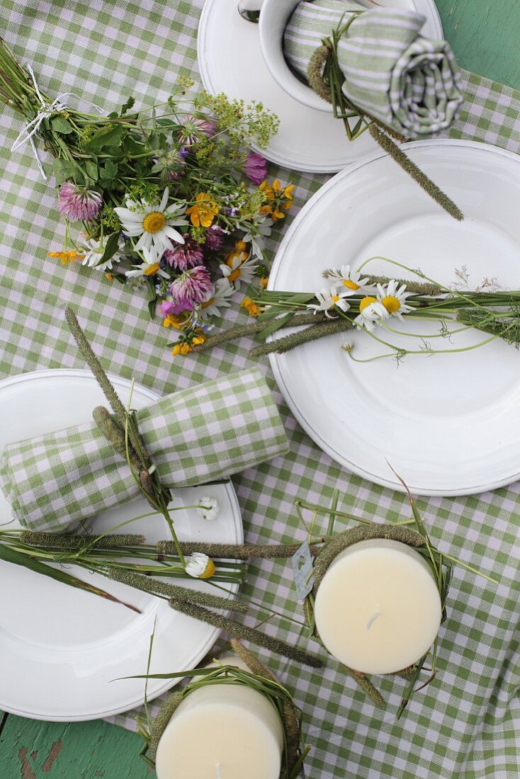 Candles and posy of wildflowers arranged on green and white gingham tablecloth