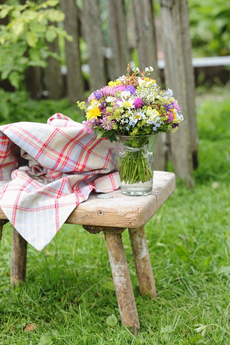 Vase of colourful wildflowers on vintage wooden stool in garden