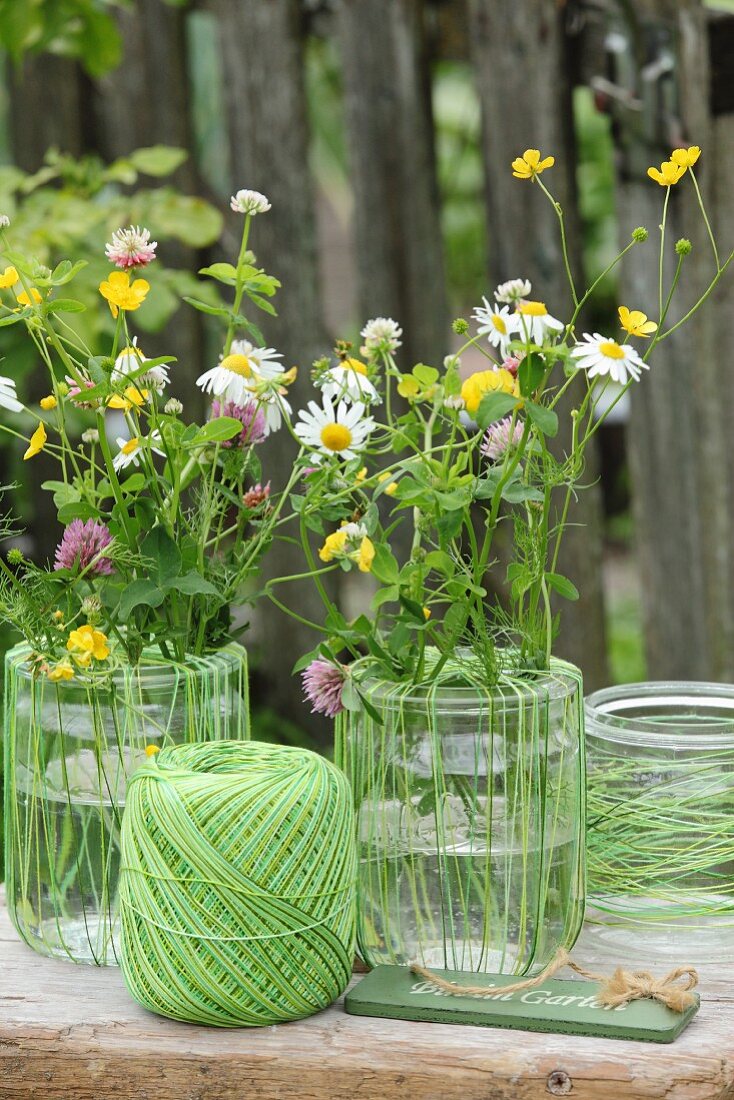 Vasendekoration mit grünem Garn und bunten Wiesenblumen