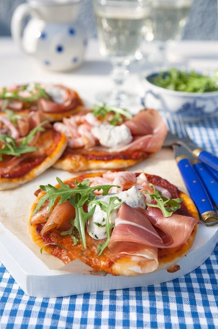 Small pizza with dried ham, tomato sauce, arugula, shrimps, smoked salmon and fresh herbs