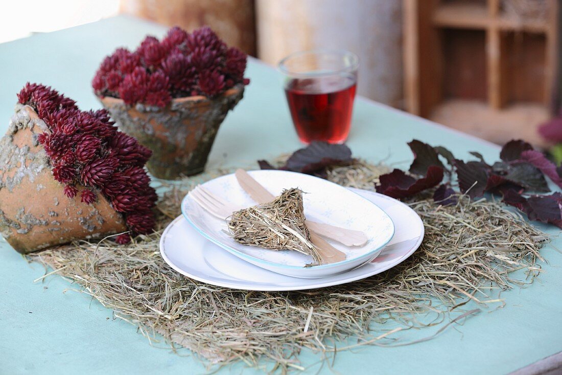 Heu-Tischset mit weißem Gedeck, Holzbesteck, Heu-Dekoherz und herbstlichem Pflanzenarrangemnt