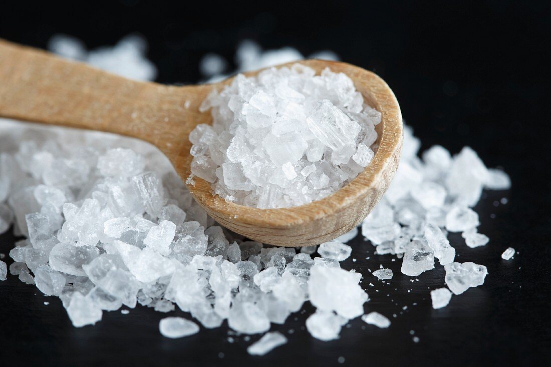 Close up of a heap of coarse salt with a wooden spoon, on black.