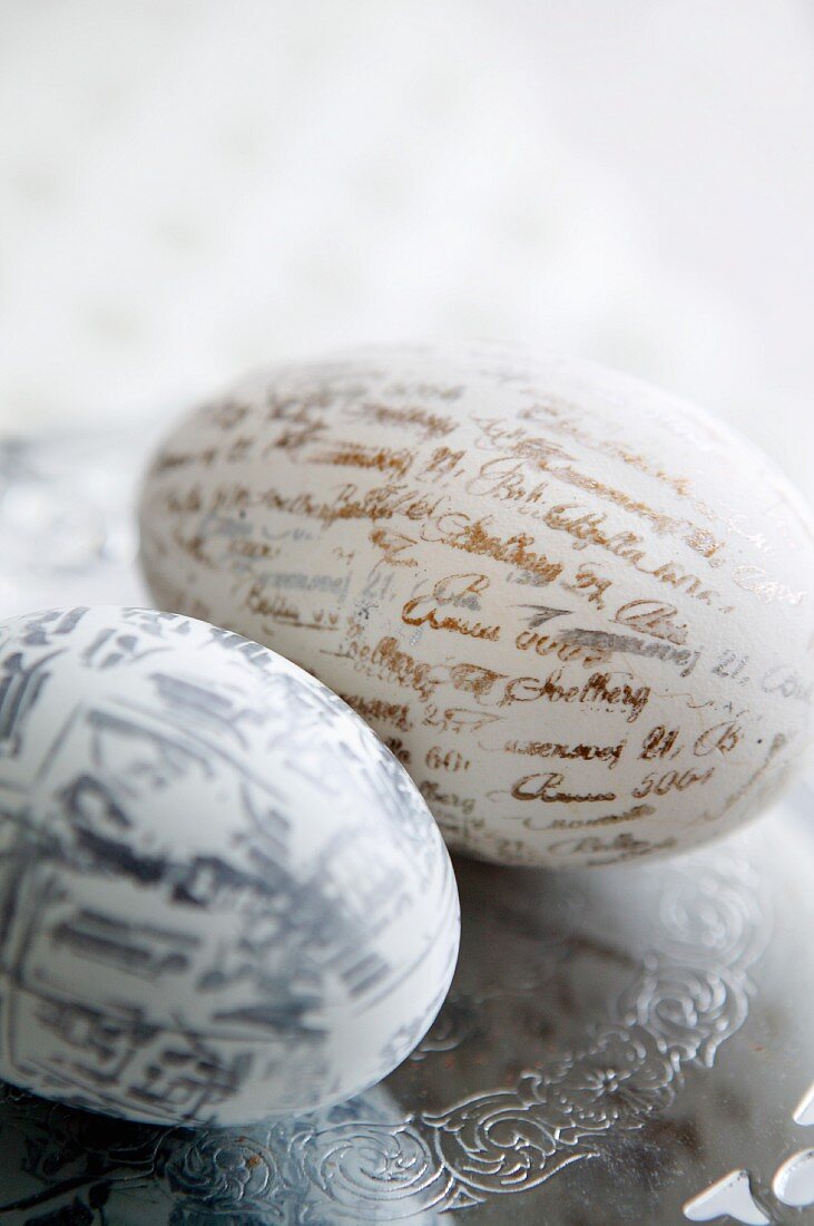 Zwei mit Schriftzügen und Schriftzeichen bedruckte Eier auf Silberteller mit Gravur