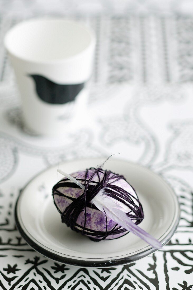 Easter egg painted purple wrapped in cord and decorated with feathers on plate