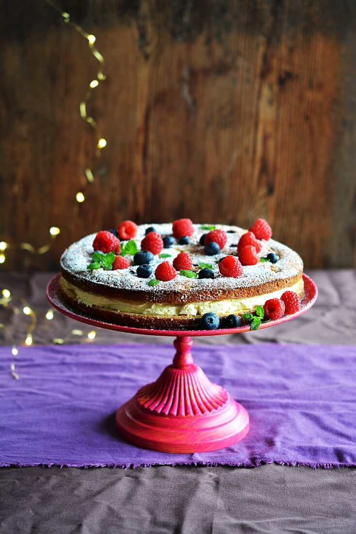 Biscuit cake with forest fruits and cream on a stand