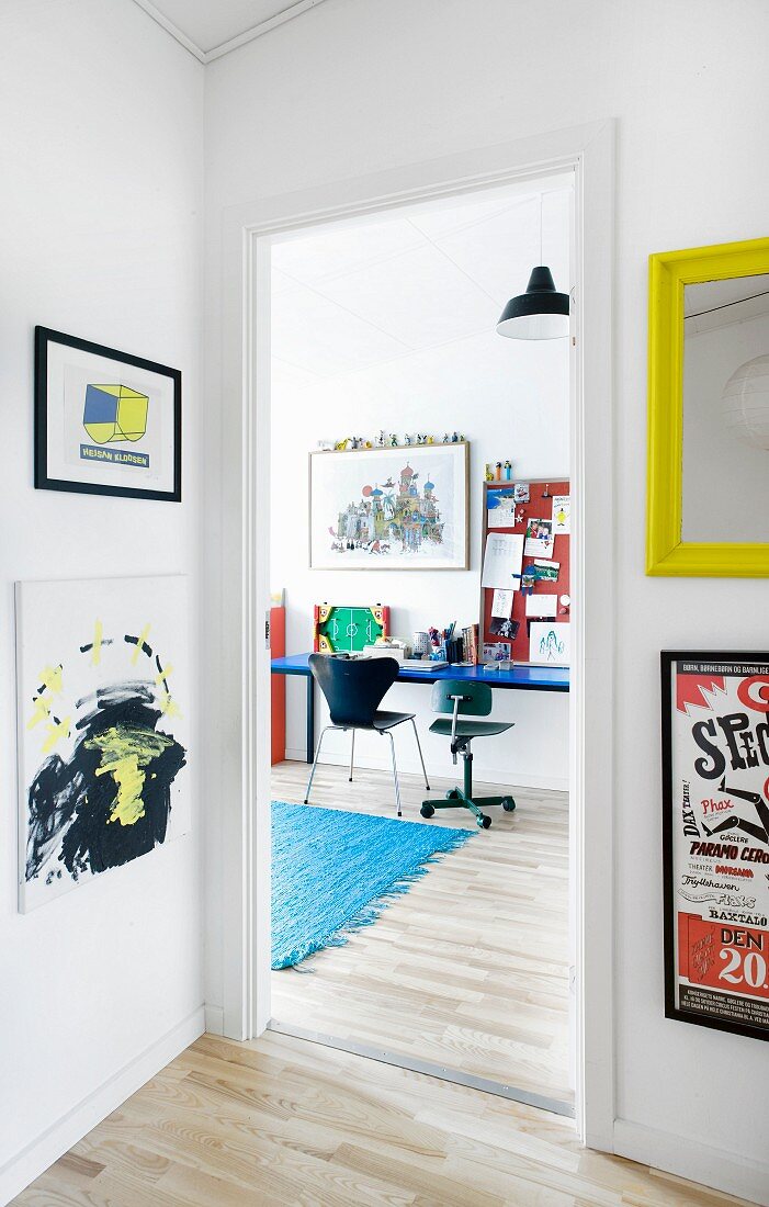Blick vom Flur mit bunten Bildern in ein Jugendzimmer mit Schreibtisch