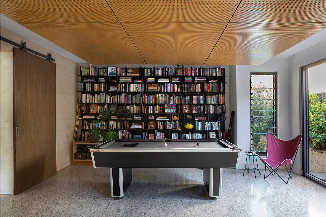 Modern pool table in front of a large bookcase under the ceiling