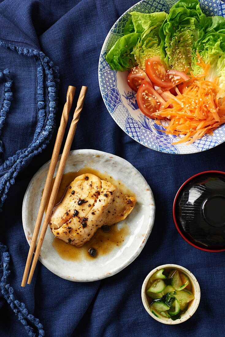 Fisch in fermentierter Bohnen-Chili-Soja-Sauce mit Miso, Salat und eingelegten Gurken