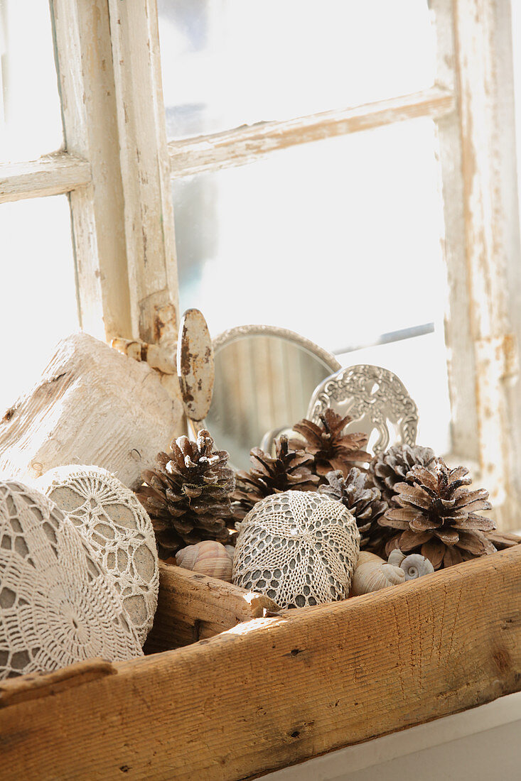 Pebbles covered with lace and pine cones in old wooden crate