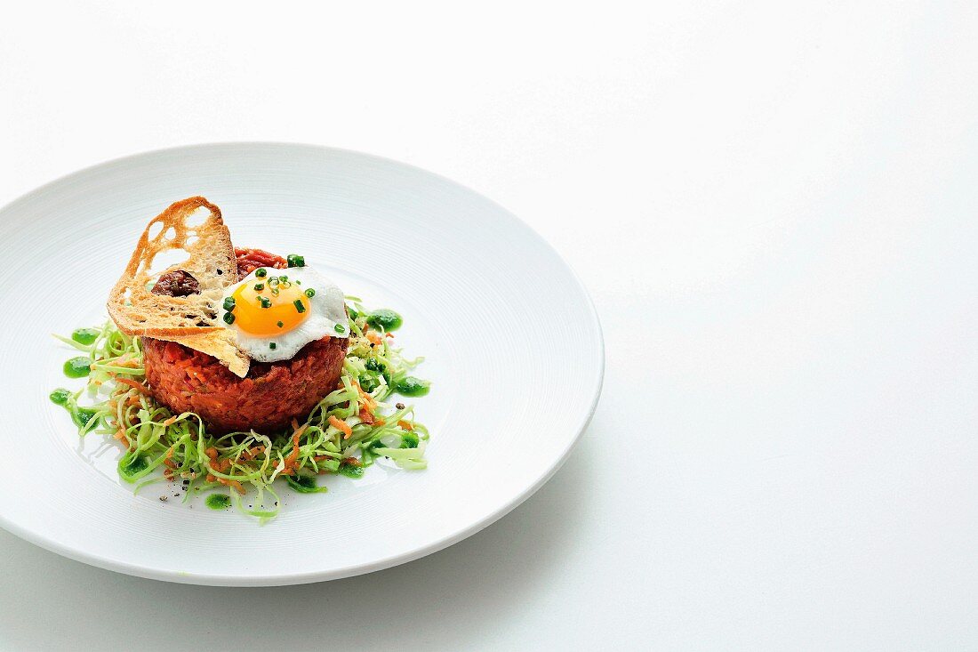 Beef tartare with a fried quail egg, a bread chip, pointed cabbage and chive oil