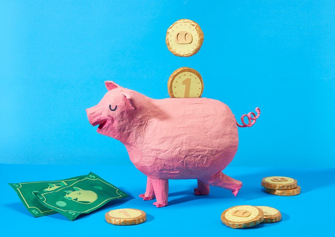 Sparschwein und Geld aus Pappmaché als Symbolbild für Sparen