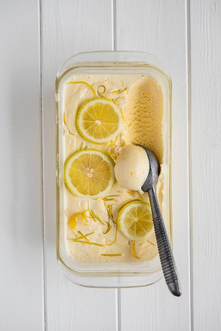 Homemade lemon ice cream in a glass tub with ice cream scoop, view from above