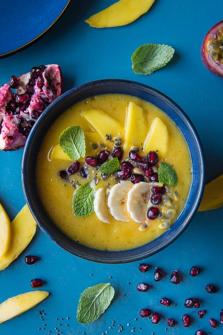 Mango and banana smoothie bowl with pomegranate seeds, passion fruit and mango slices