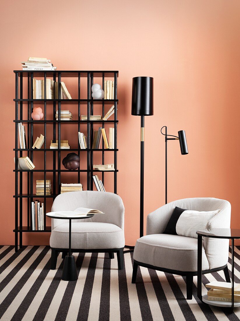 Two pale armchairs on black and white rug in front of bookcase and pink wall