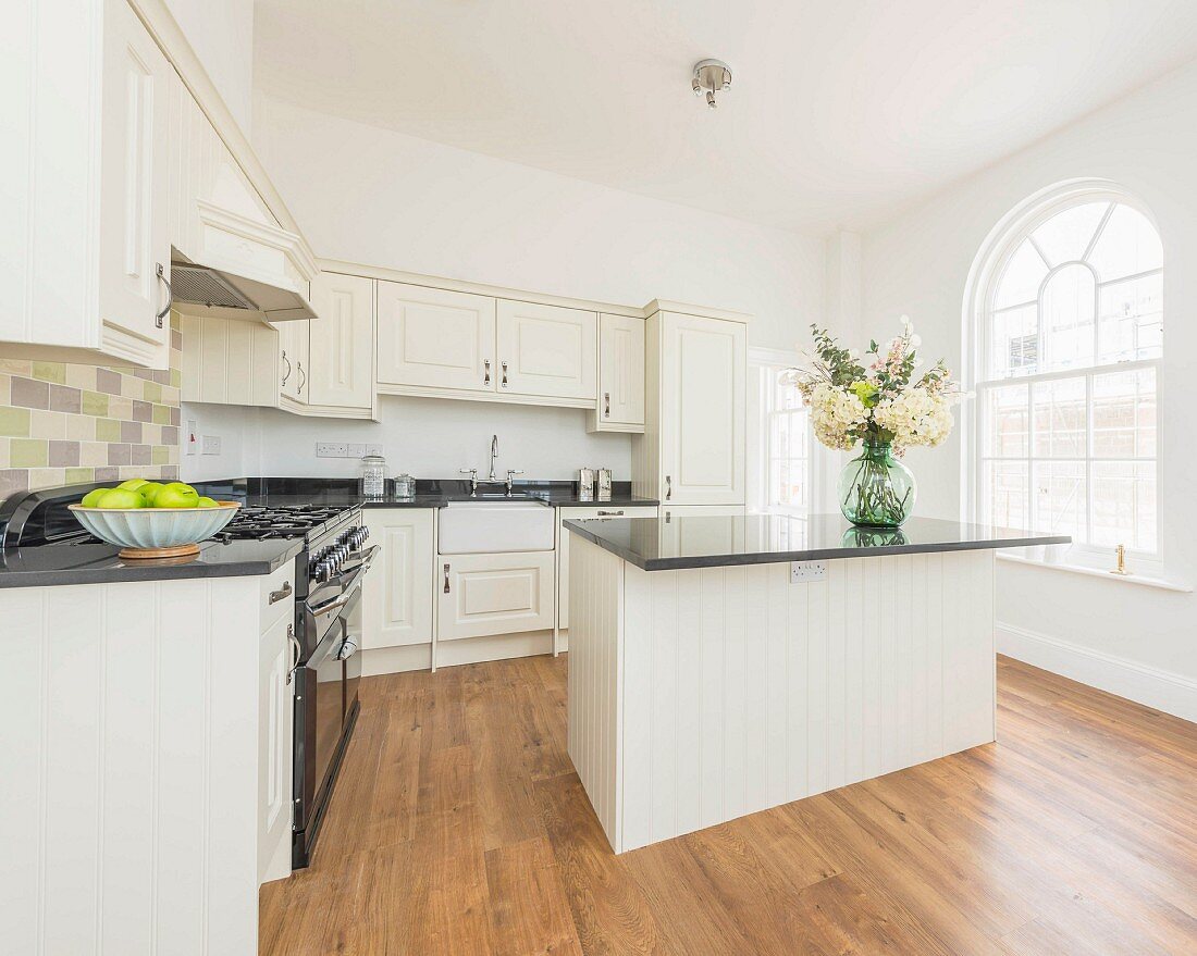 A natural white country house kitchen with a breakfast bar in an old building with round arch windows